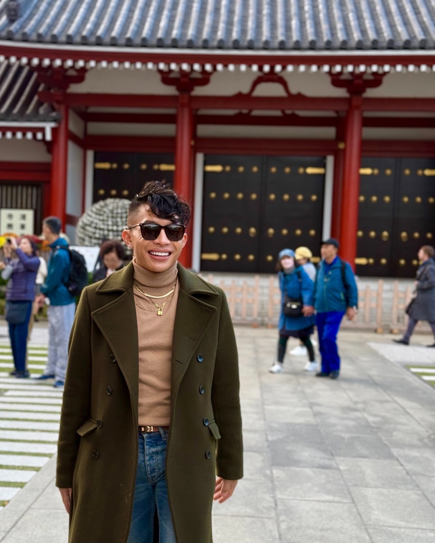 Beatus smiling in an olive overcoat and sunglasses in front of the red pillars of Senso-ji temple